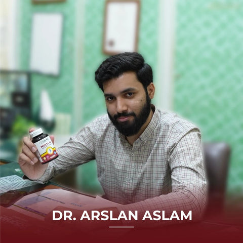 Dr. Arslan Aslam holding NHC Multi-W One-A-Day Women multivitamin supplement bottle at his desk