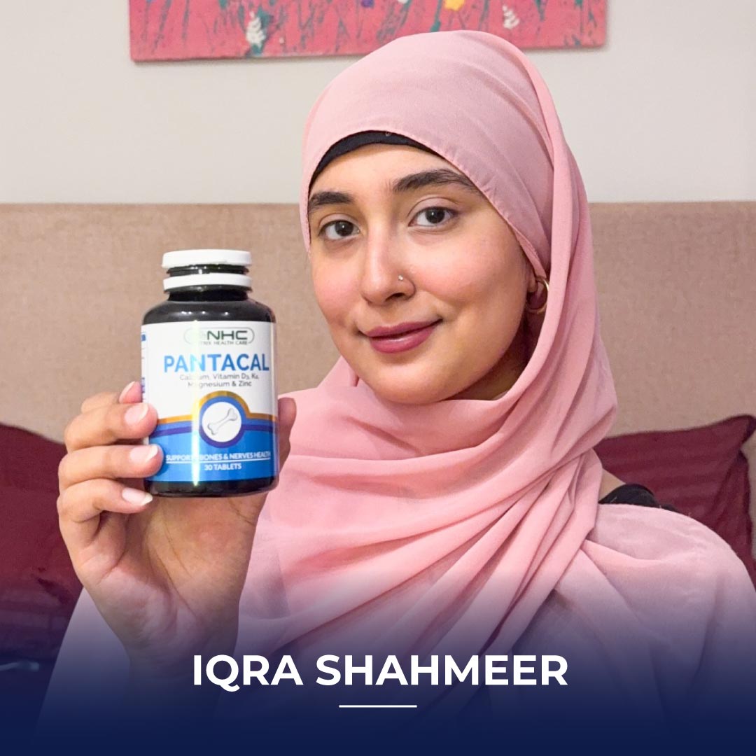 Iqra Shahmeer wearing a pink hijab, holding a bottle of Pantacal supplement while sitting at home