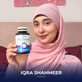 Iqra Shahmeer wearing a pink hijab, holding a bottle of Pantacal supplement while sitting at home