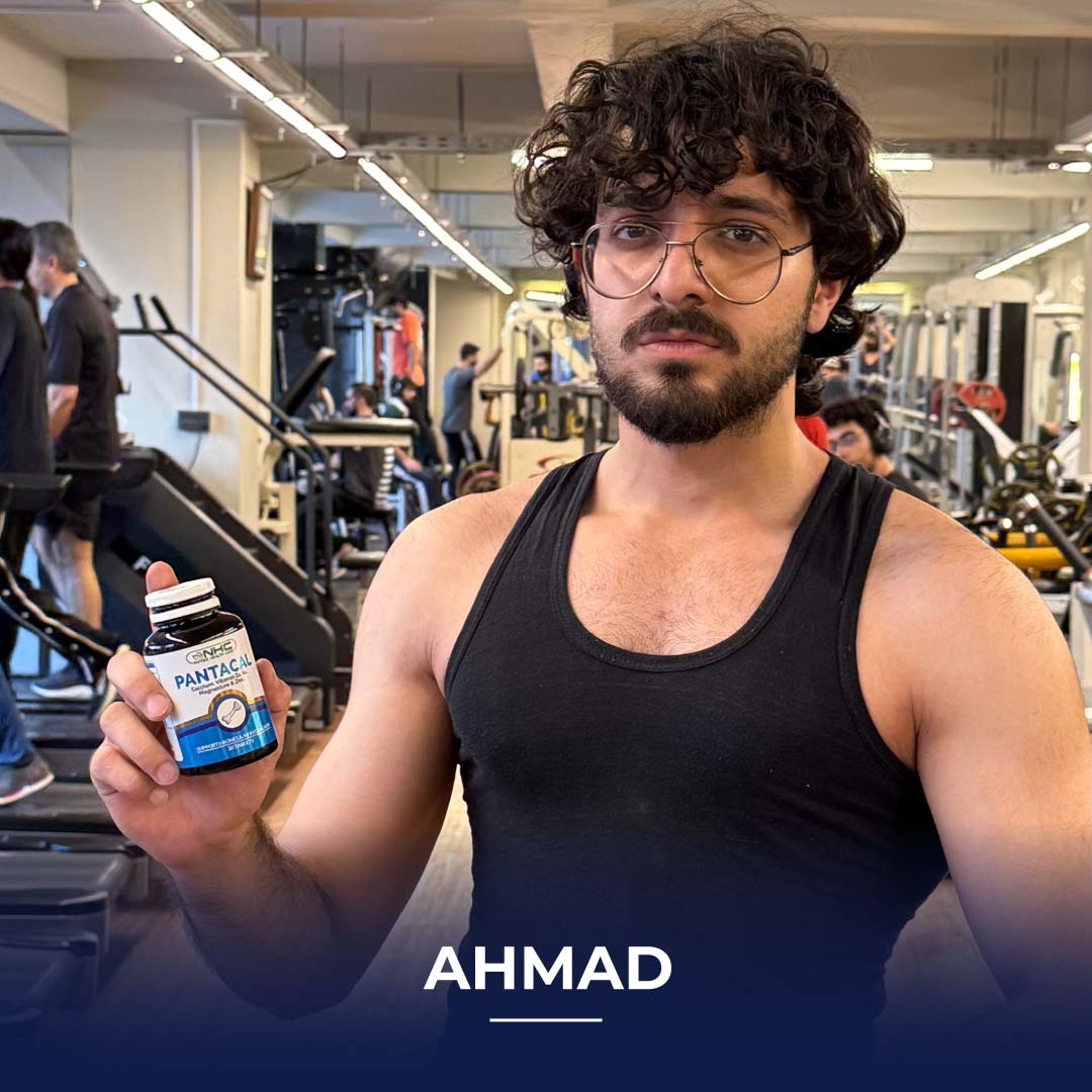 Ahmad, a young man in a black tank top and glasses, holding a bottle of Pantacal supplement inside a gym