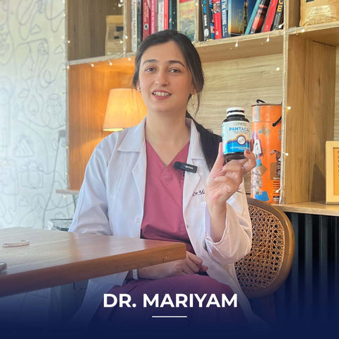 Dr. Mariyam, a doctor in a white lab coat and pink scrubs, holding a bottle of Pantacal supplement in a cozy café/library setting